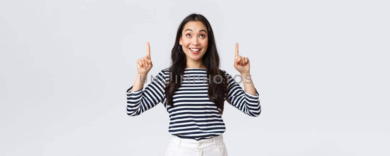 Lifestyle, people emotions concept. Excited good-looking asian girl smiling pleased as found excellent product, pointing fingers up at advertisement and looking satisfied, recommend promo.