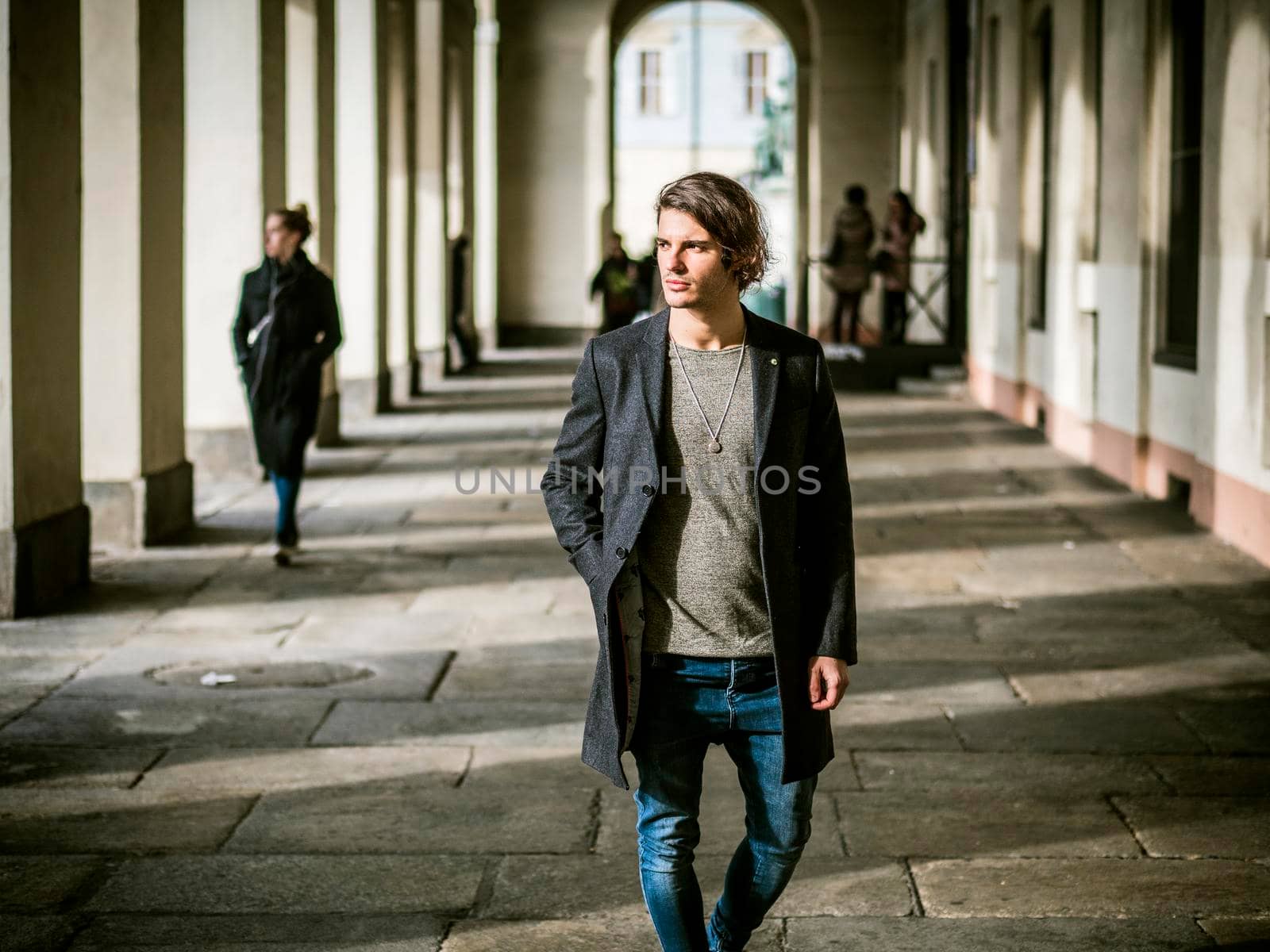 Elegant attractive young man outdoor wearing wool coat, in European city under colonnade in city center