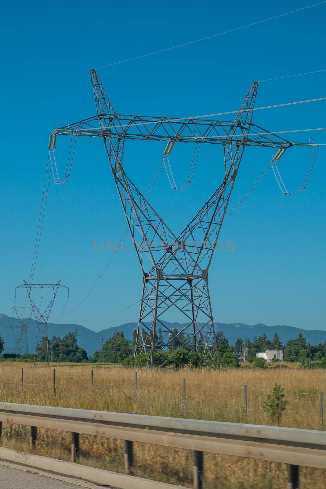 High voltage pole with blue sky, blue sky, trees and grass.