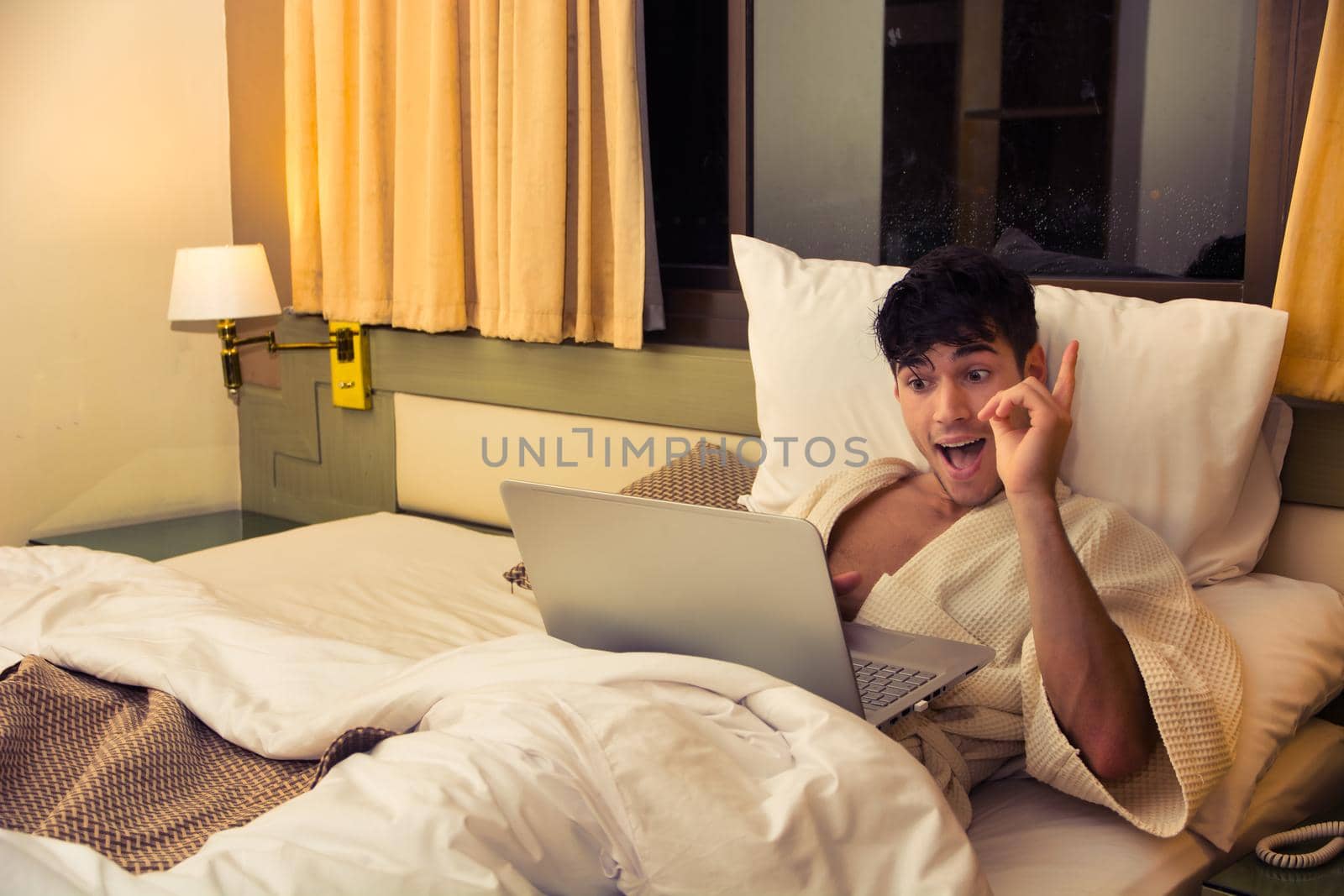 Attractive Young Shirtless Muscular Man with Serious Expression, Reclining Comfortably with Laptop on Bed Working on his Start-up Business - Young Male College or University Student Doing Homework, in Bedroom Looking at Camera