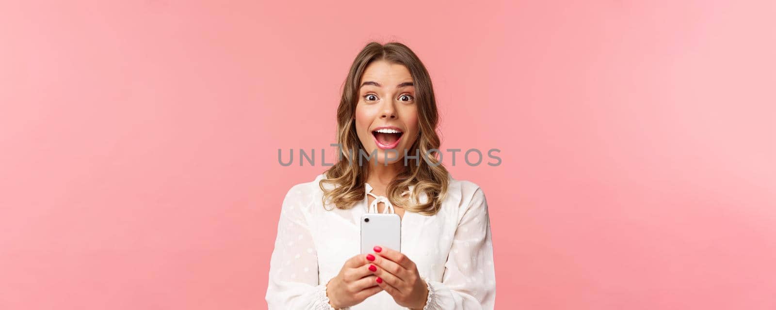 Close-up portrait of excited and amazed young blond girl attend performance of favorite singer, record video, stream online on mobile phone, taking photo with smartphone, look thrilled.