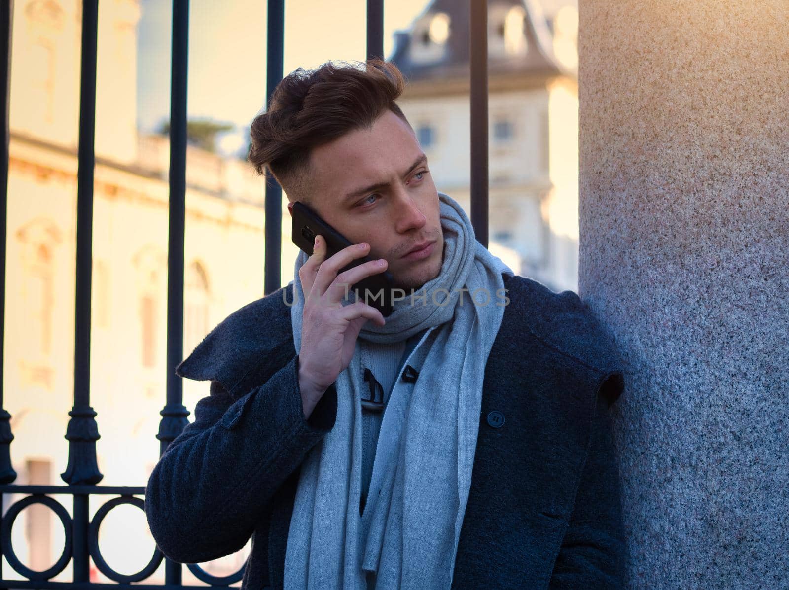 Handsome trendy man wearing white shirt standing and talking on cell phone, outdoor in city setting in day shot
