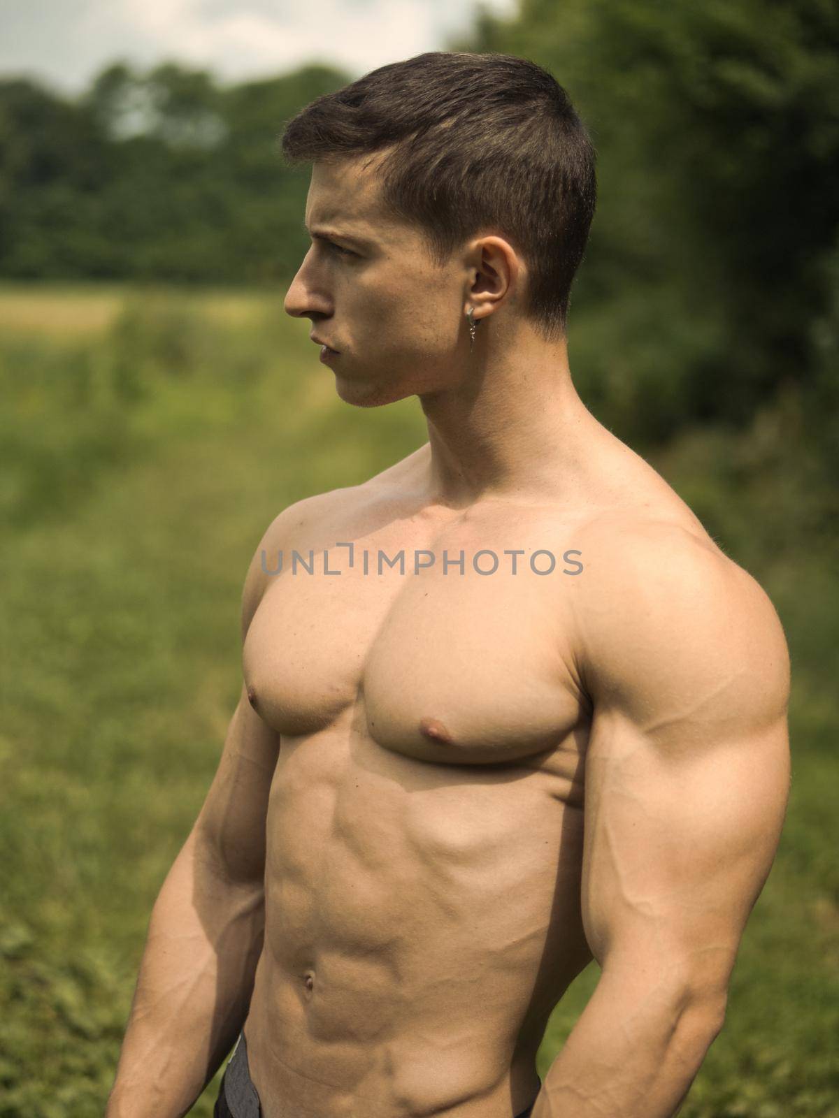 Handsome Muscular Shirtless Young Hunk Man Outdoor in Nature Standing on Grass. Showing Healthy Muscle Body While Looking away