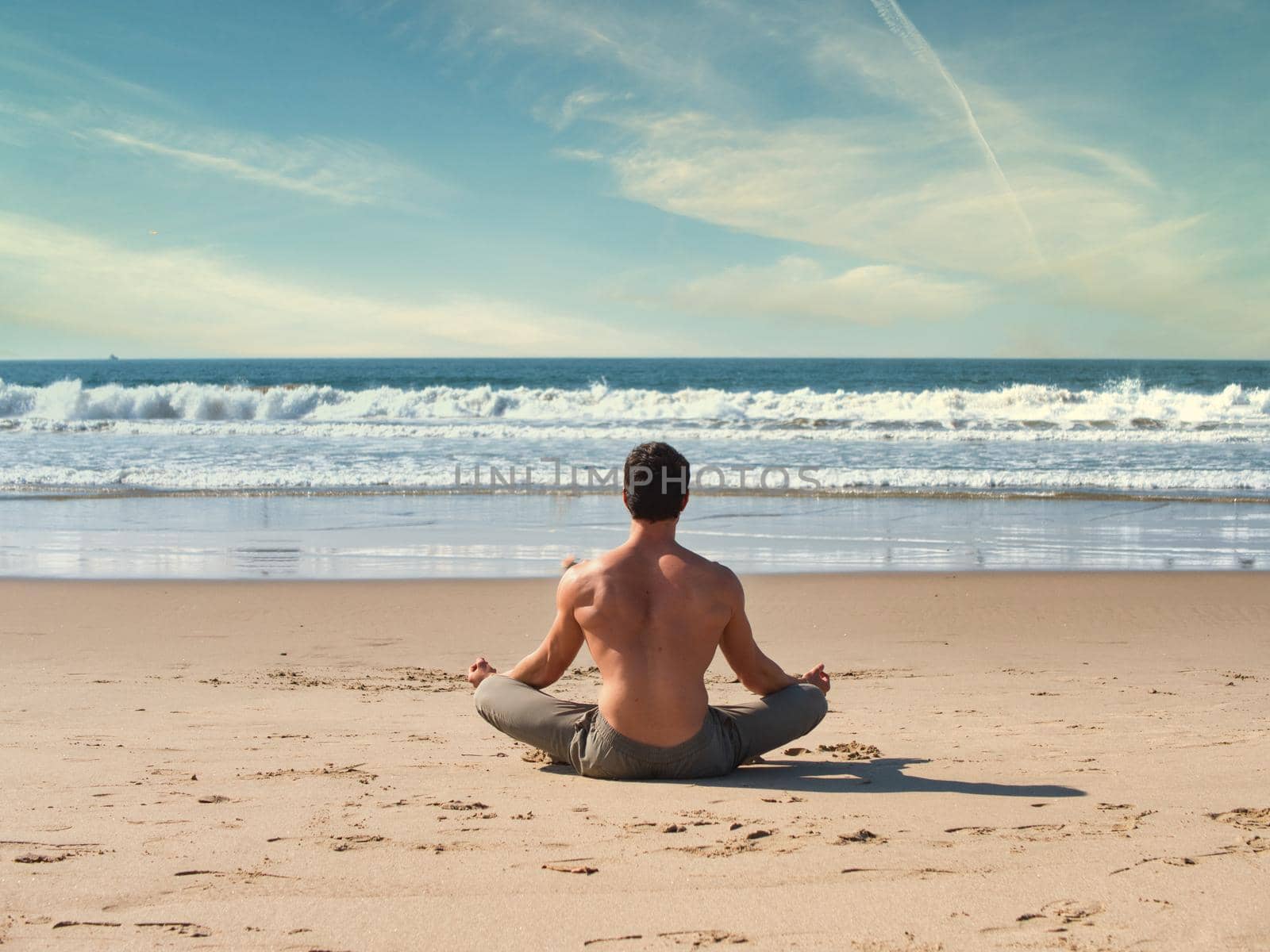 Fit Shirtless Young Man During Meditation or Doing an Outdoor Yoga Exercise Sitting on Rocks by Ocean Shore