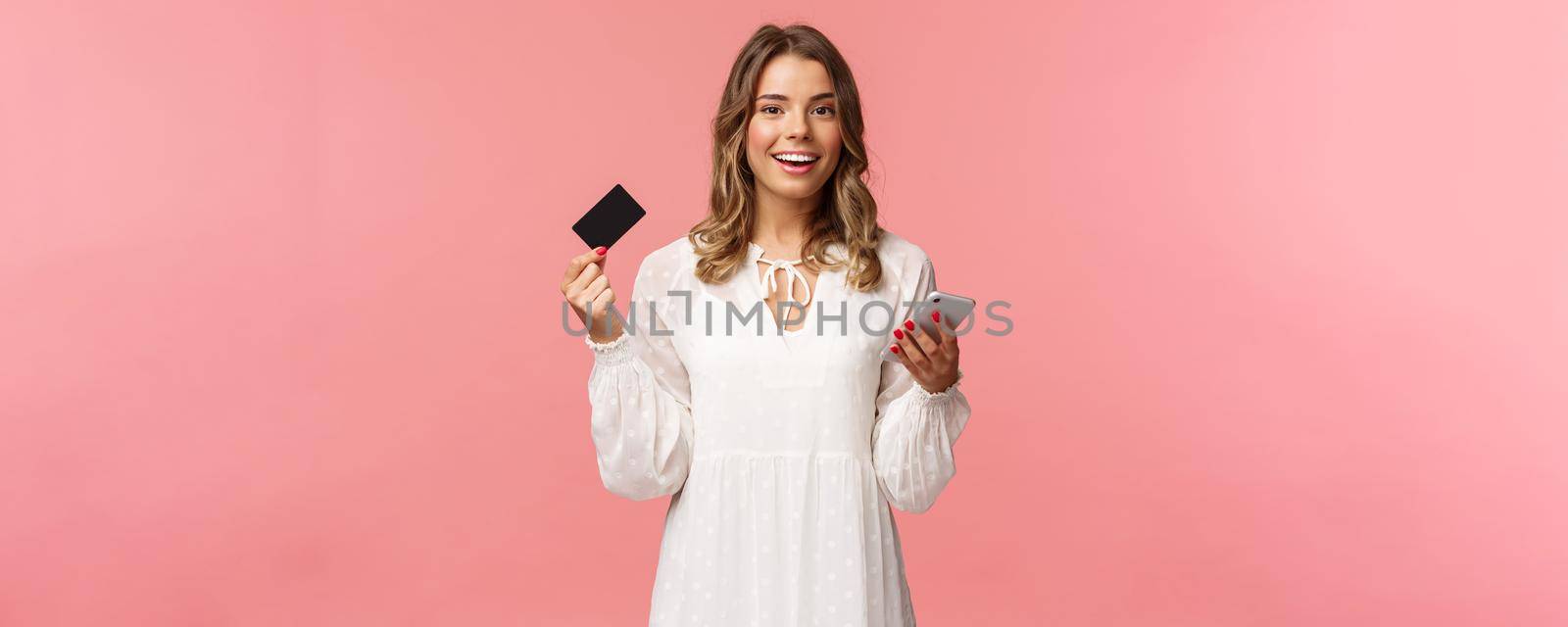 Portrait of carefree young pretty blond woman using mobile phone to pay for online purchase, holding credit card and smiling happy camera, shopping internet, download smartphone app.