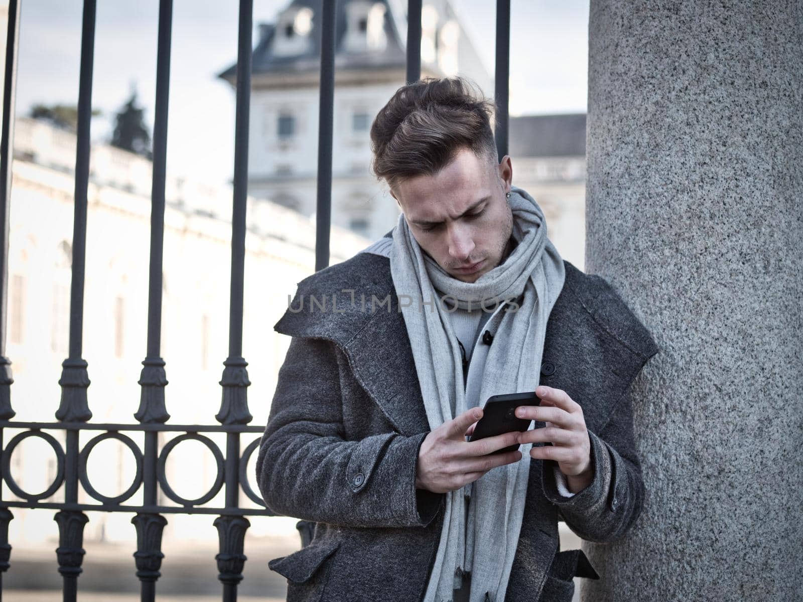 Handsome trendy man wearing cardingan standing and typing on cell phone, outdoor in city setting in day shot
