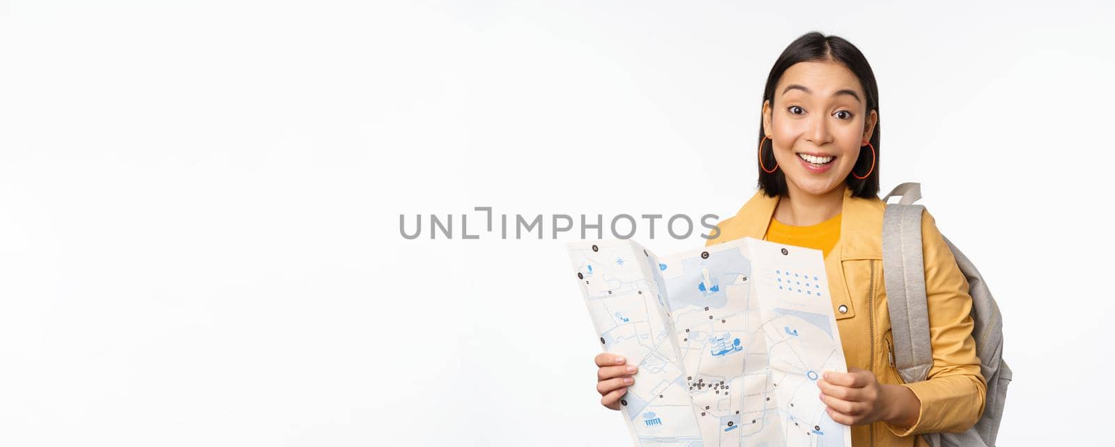 Image of young asian girl tourist, traveller with map and backpack posing against white studio background. Copy space