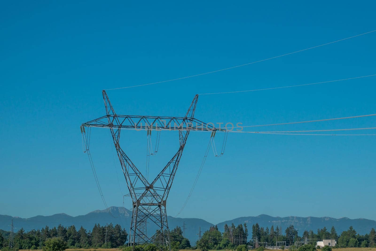 High voltage pole with blue sky, blue sky, trees and grass.