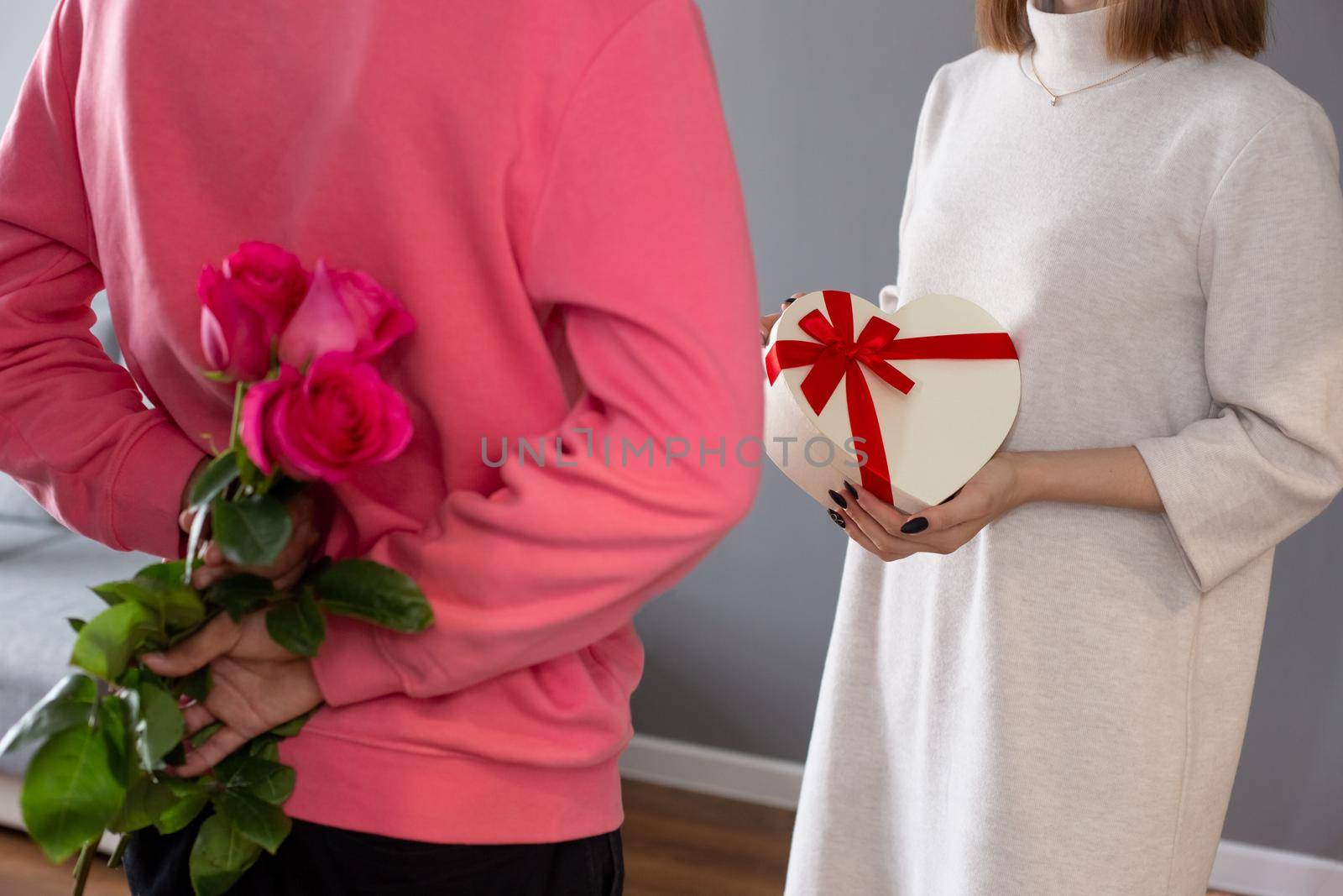 A guy in a pink jumper, holding a bouquet of roses behind his back and a girl in a white dress, holding a white box in the form of a heart. close-up, no face