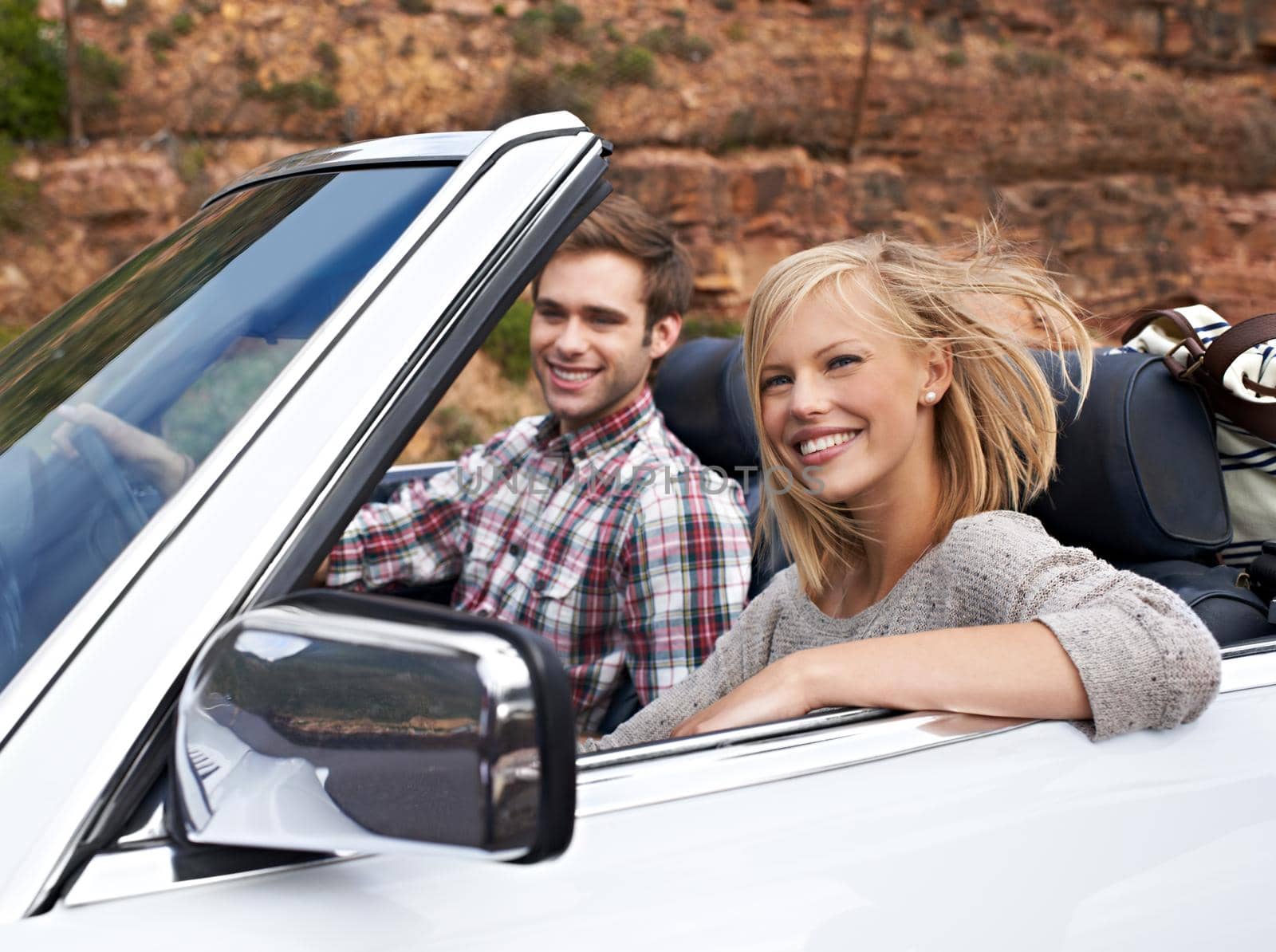 We love our weekend getaways. Shot of a young couple enjoying a drive in a convertible. by YuriArcurs