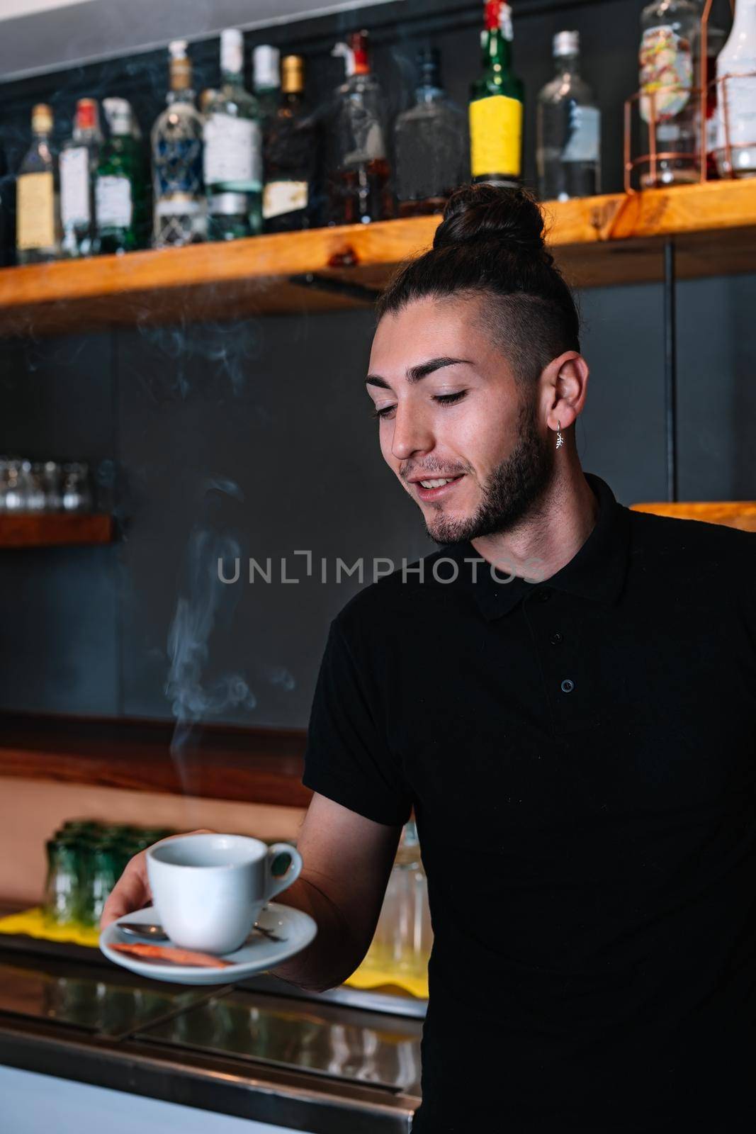 young smiling waiter man serving coffee in a white cup. vertical by CatPhotography