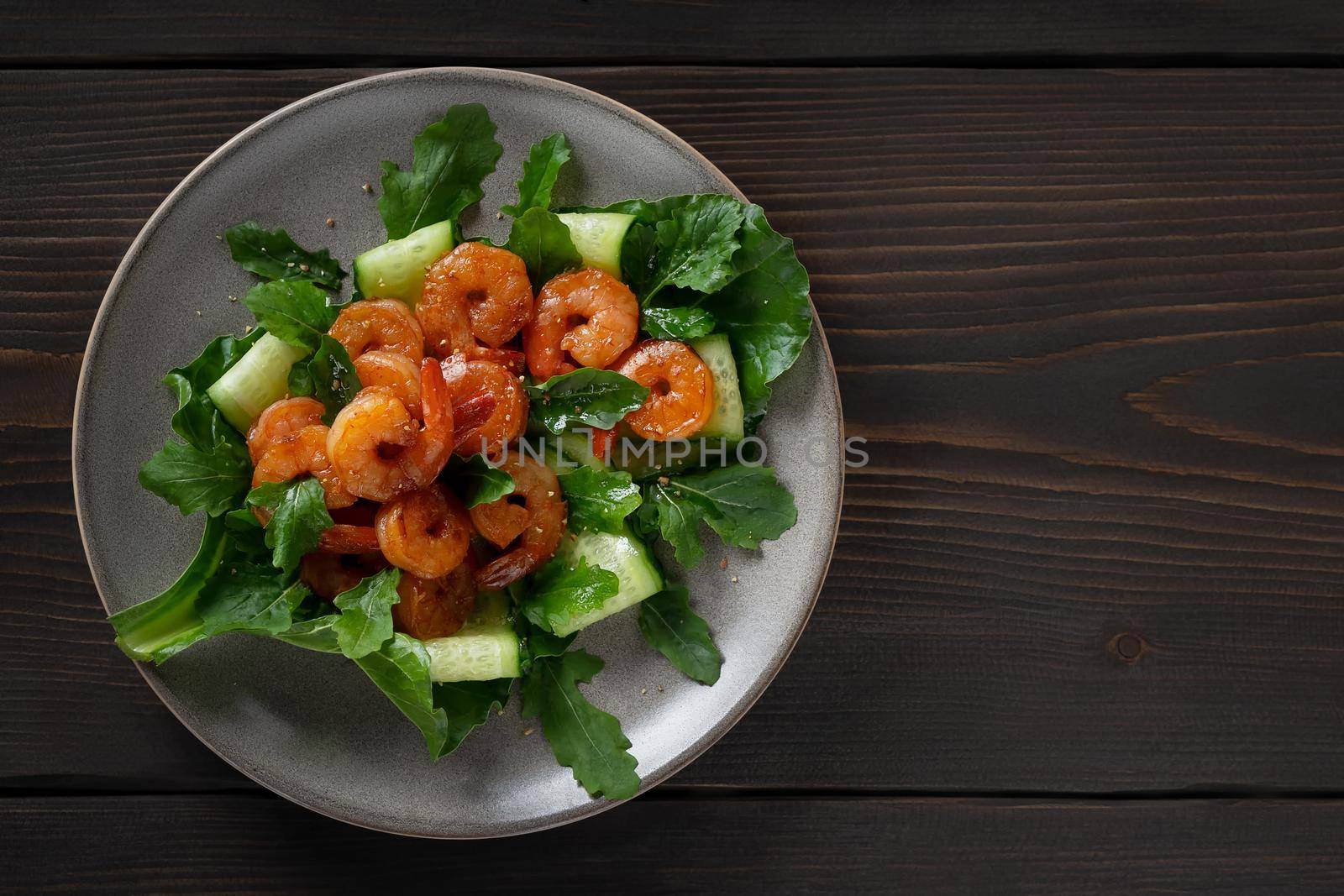 Fresh salad with grilled shrimps, cucumbers and arugula beautifully served on a plate, top view, flat lay.