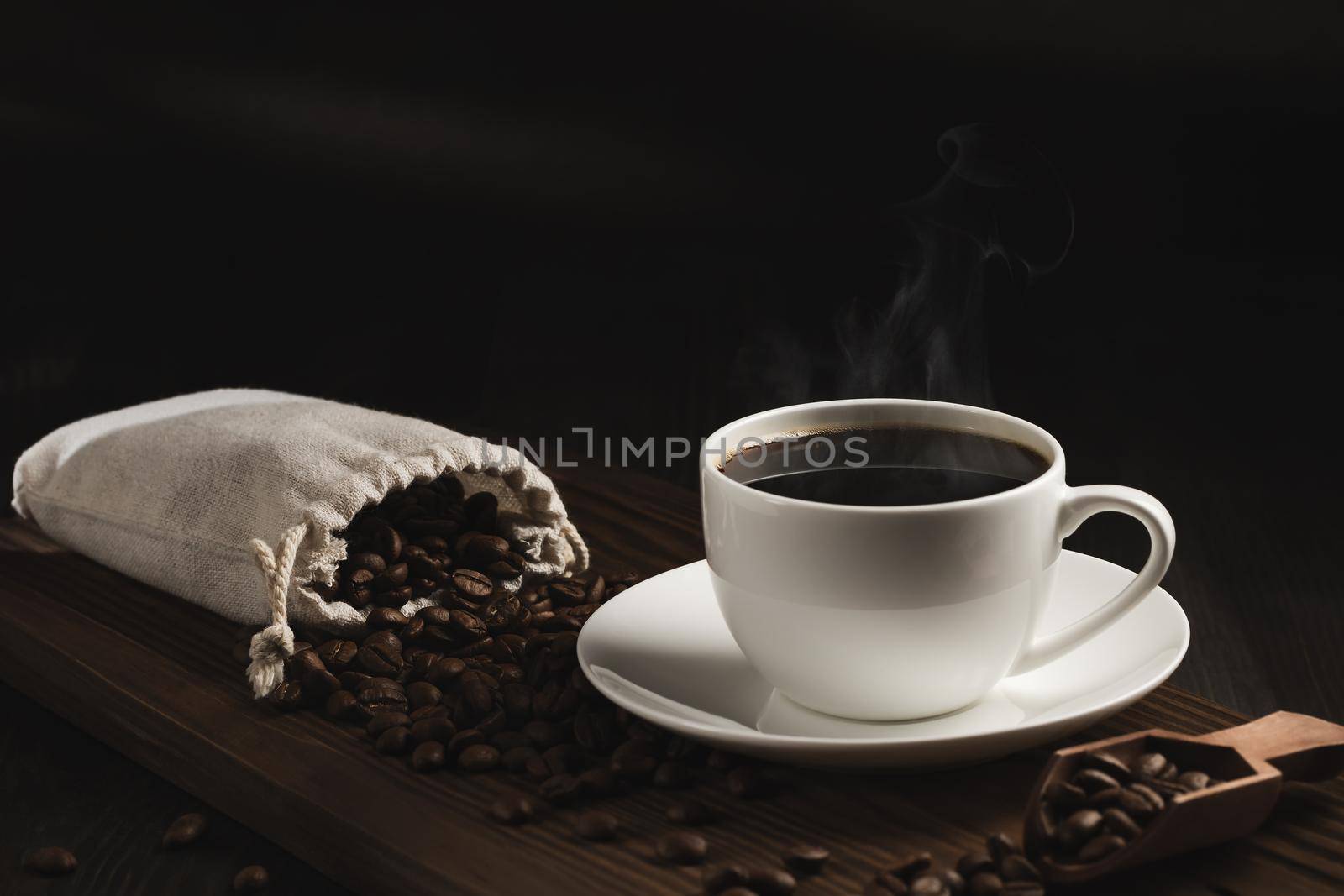 White cup of fresh hot coffee and coffee beans on wooden board on table.