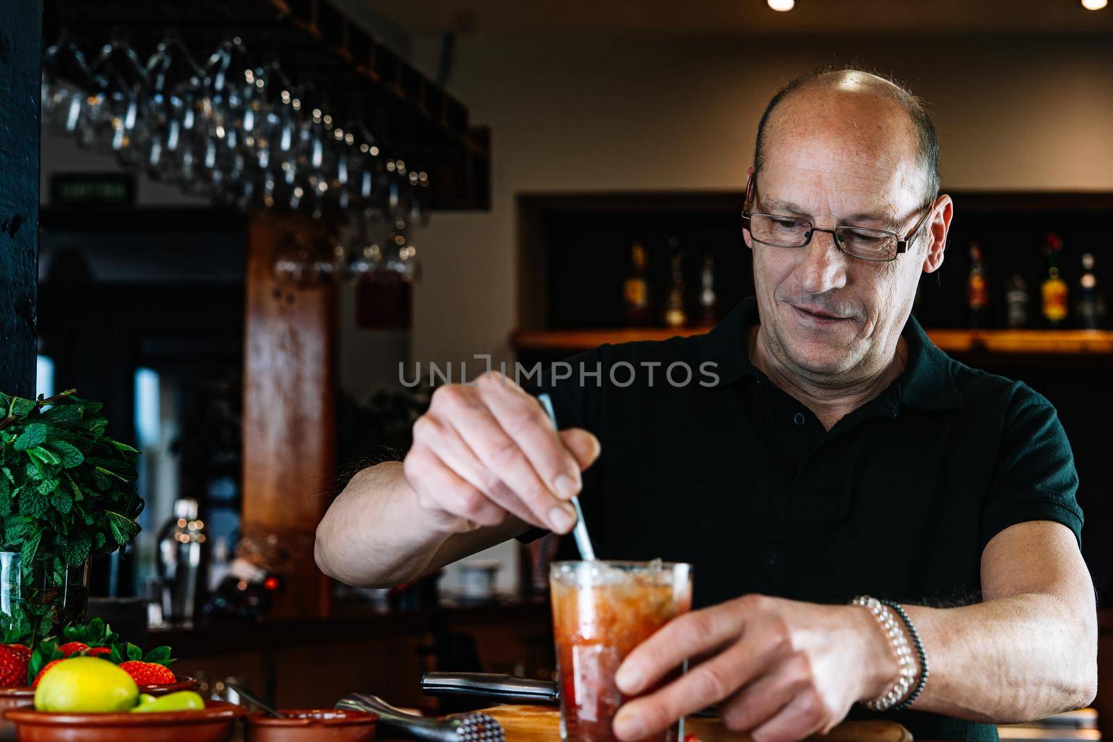 Experienced bartender shaking a cocktail in a crystal glass. Preparing a cocktail for the customers by CatPhotography