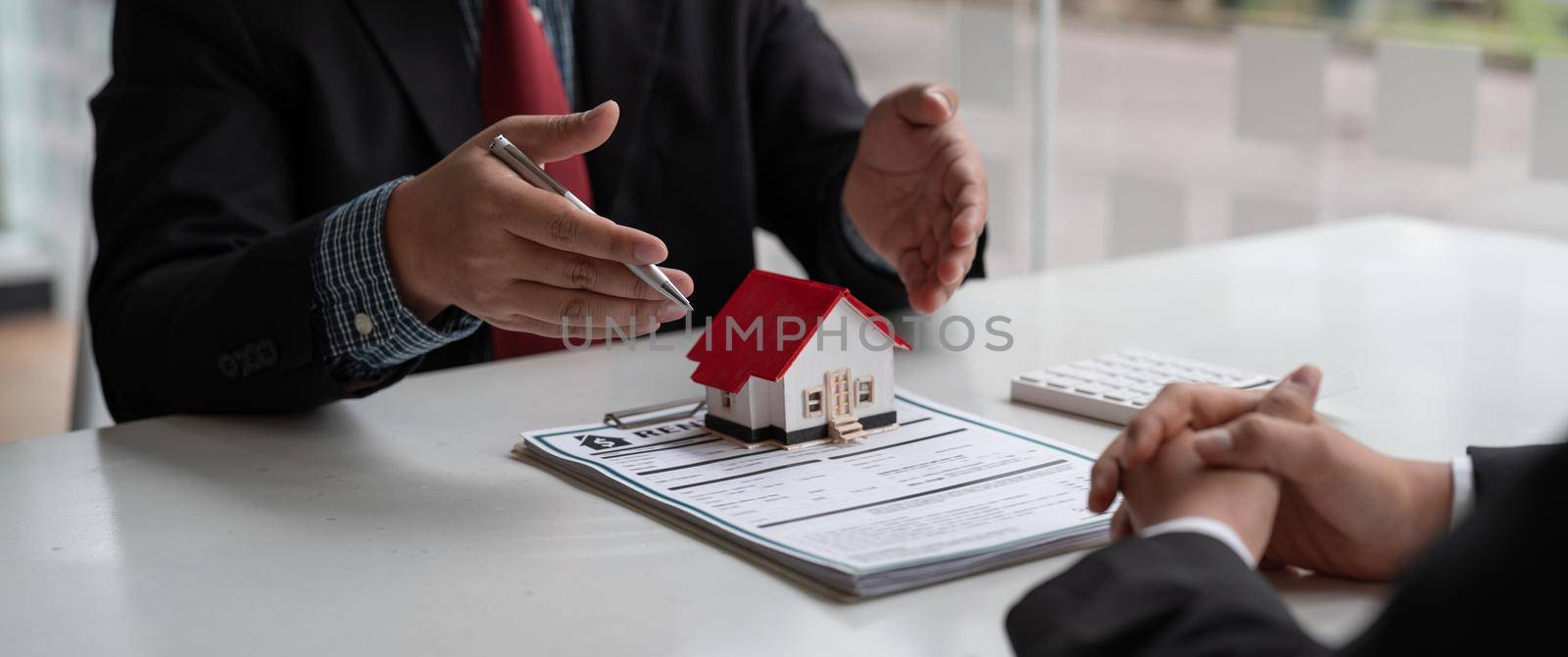 Real estate concept - businessman offer to signs contract with home architectural model at his office.