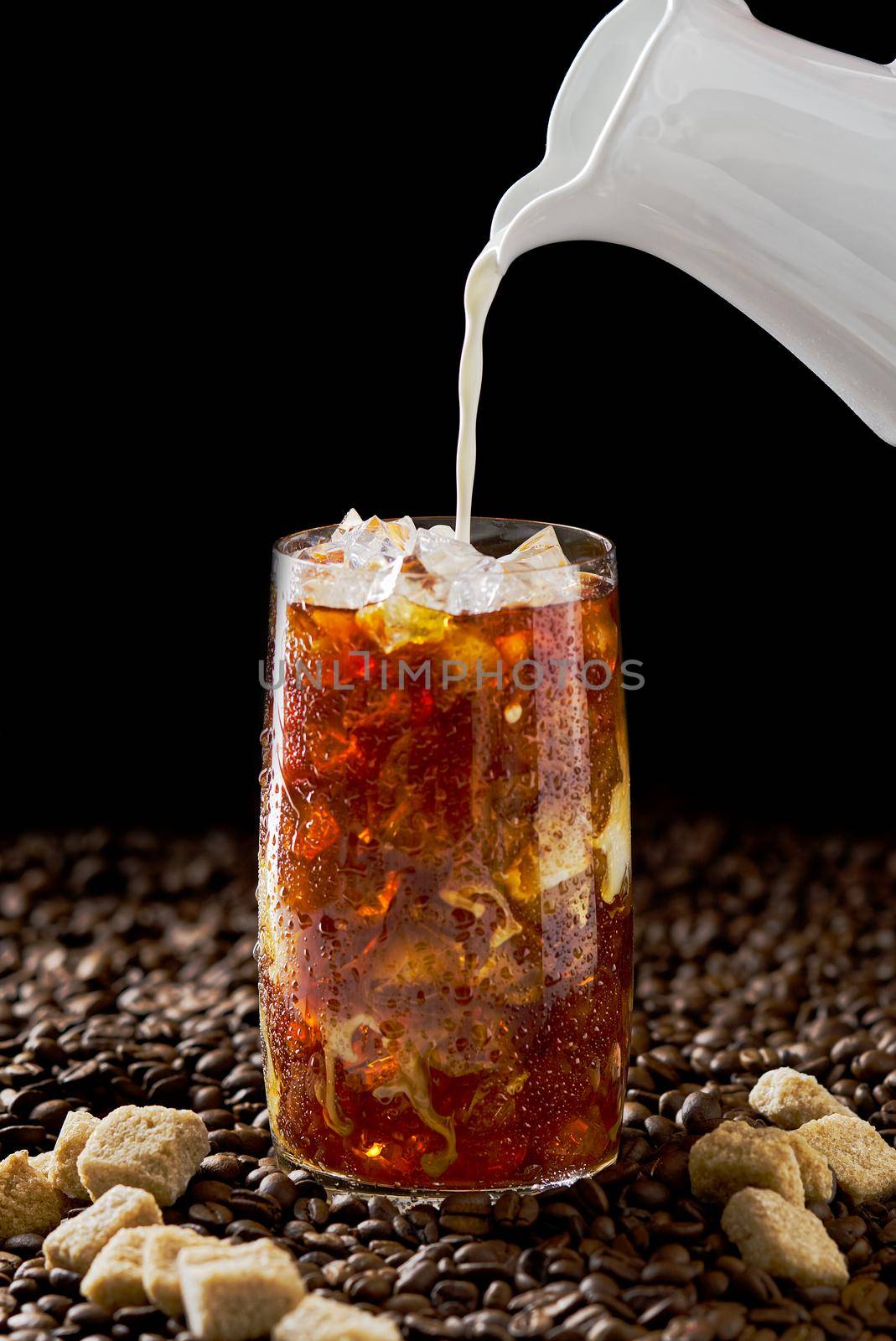 Iced coffee. Tasty ice coffee with milk, cold drink in glass with ice on dark coffee background. by PhotoTime