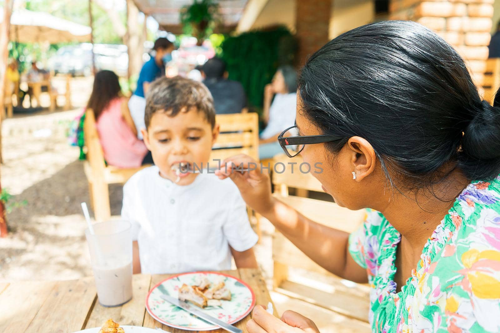 Latin woman feeding her son with a fork pieces of chicharron in a traditional Central American food restaurant