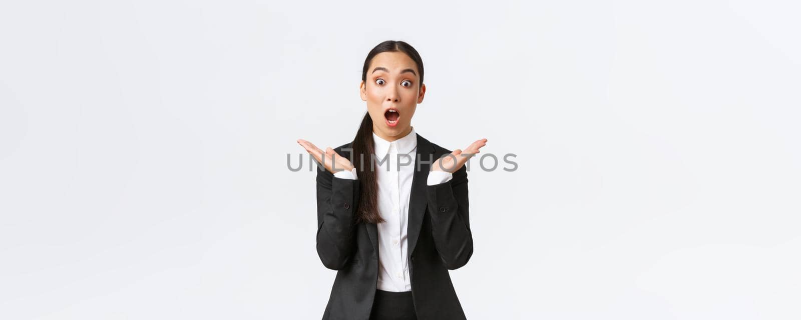 Surprised and happy female team lead, manager in office wearing suit and clap hands amazed, hear great news, amazing win. Asian entrepreneur standing pleased, reacting to success.