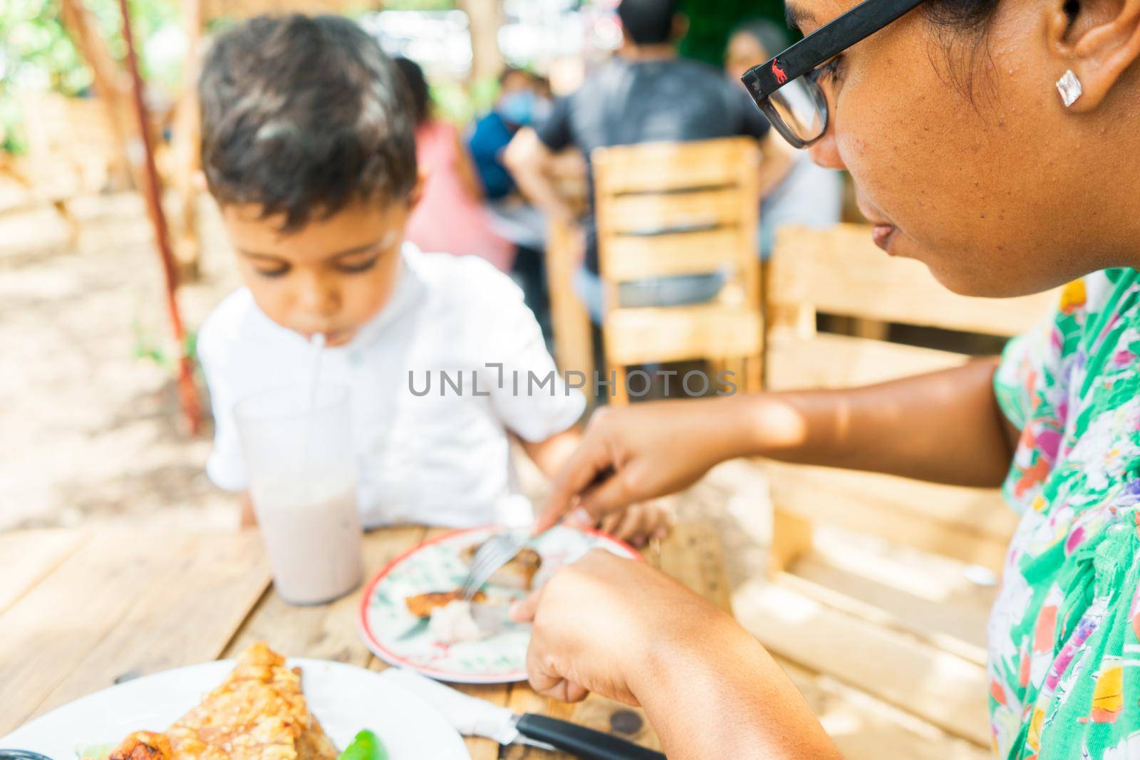 Latin woman cutting pieces of chicharron to feed her son in a traditional Central American food restaurant