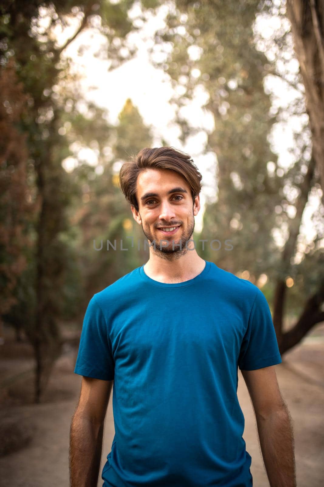 Vertical portrait of smiling young man standing in the forest looking at camera. Lifestyle concept.
