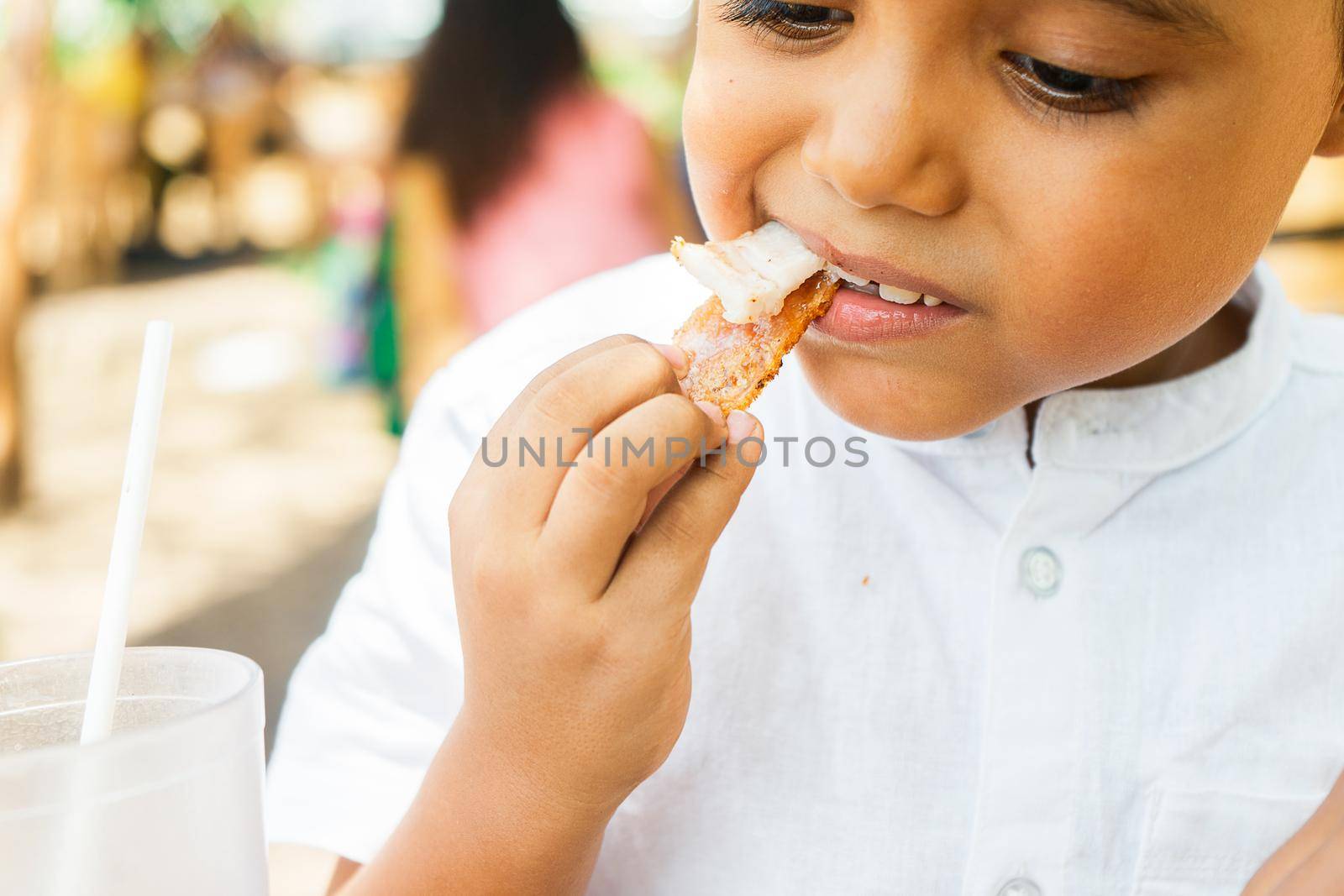 Latin boy biting a piece of chicharron in a traditional Central American food restaurant