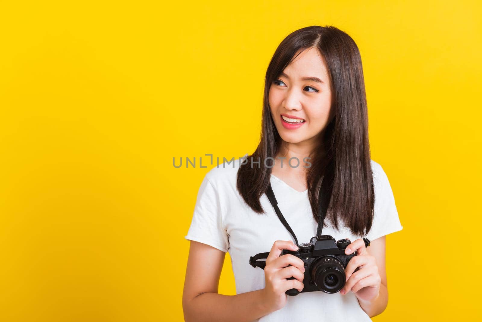 Portrait of happy Asian beautiful young woman photographer holding vintage digital mirrorless photo camera on hands, studio shot isolated on yellow background, lifestyle teenager hobby travel concept