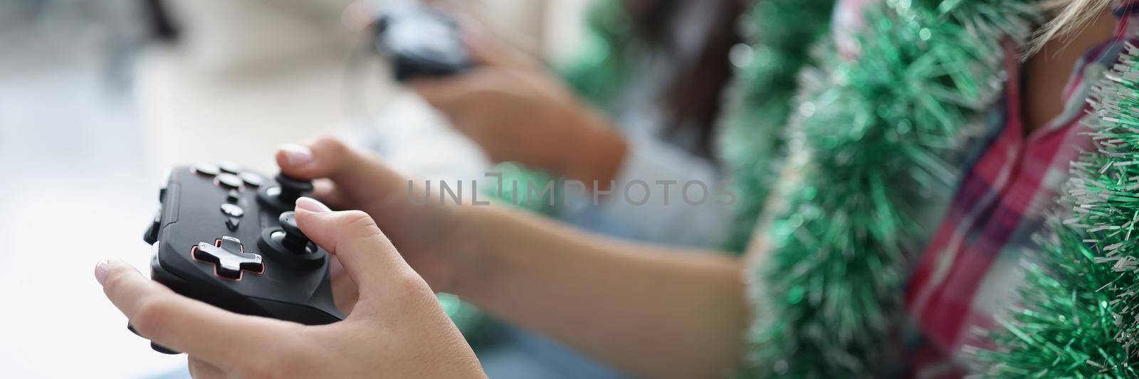 Close-up of people pressing buttons on joystick, playing video games for fun, killing time on weekend, wearing festive decor. Funny pastime, hobby, addiction, leisure, new year concept