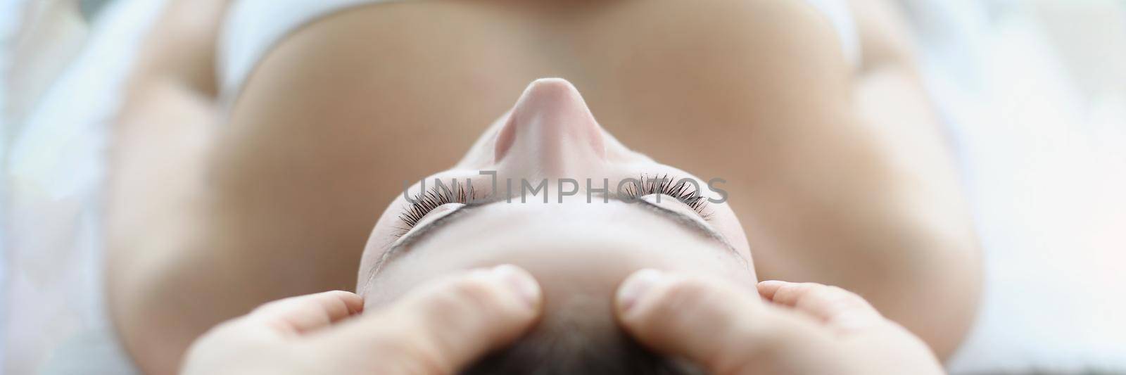 Close-up of professional masseuse giving head massage to client. Woman relaxing on towel in luxury spa centre, total relaxation and calm atmosphere. Massage, spa, wellness, body care concept