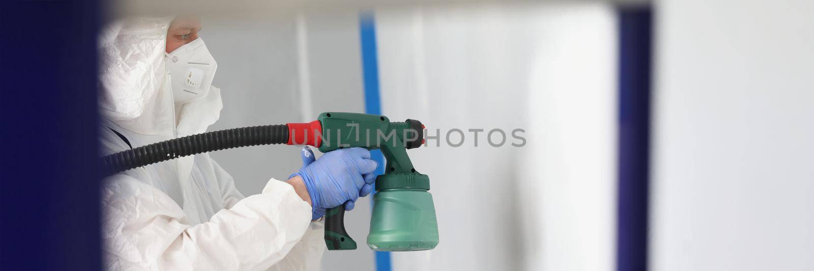 Close-up of worker painting wall with spray gun in white colour. Effective way to paint walls. Renovation, construction, interior design, household repair concept