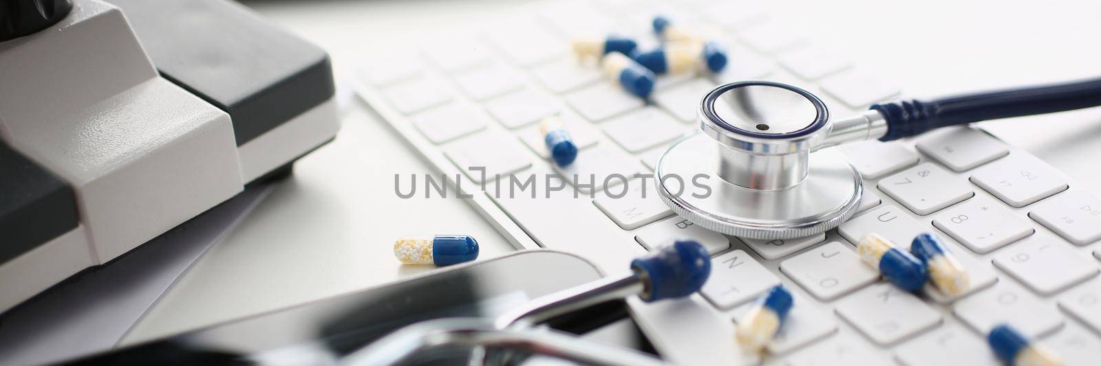Close-up of medical worker desk, mess on working place, stethoscope tool, scattered pills on keyboard, locked tablet screen. Chaos, messy, slovenliness, medicine, office concept