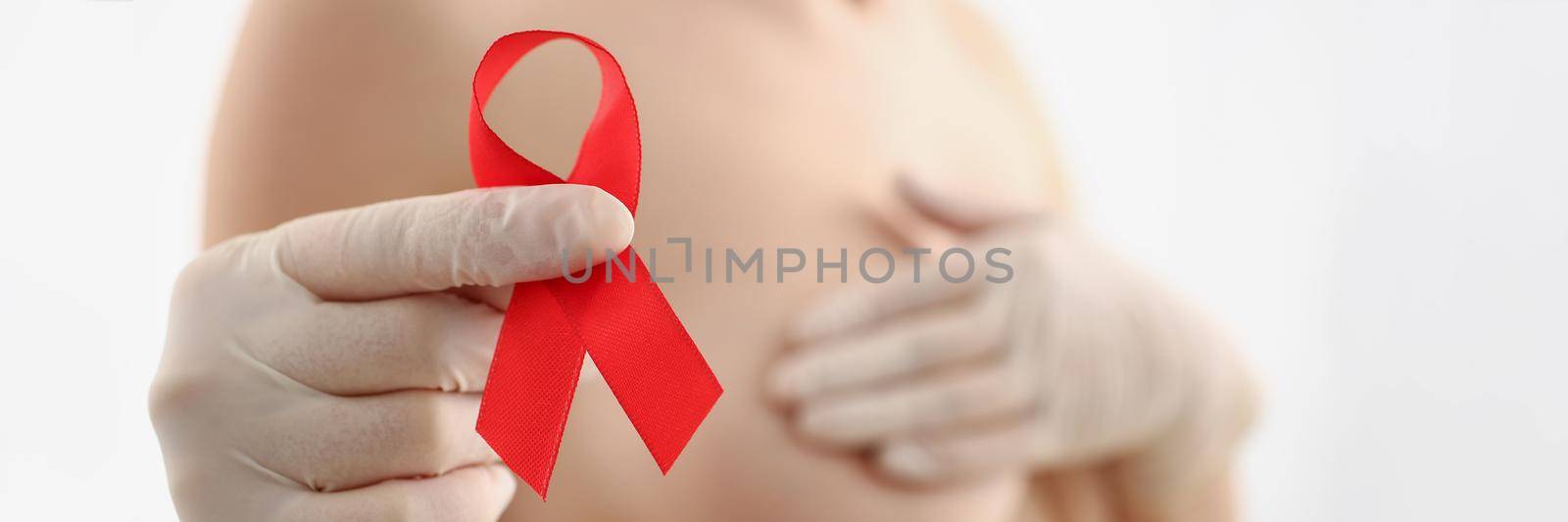 Close-up of woman holding red ribbon, fight breast cancer, support female in fighting illness. Topless female on blurred background. Breast cancer, disease, medicine, diagnostics concept