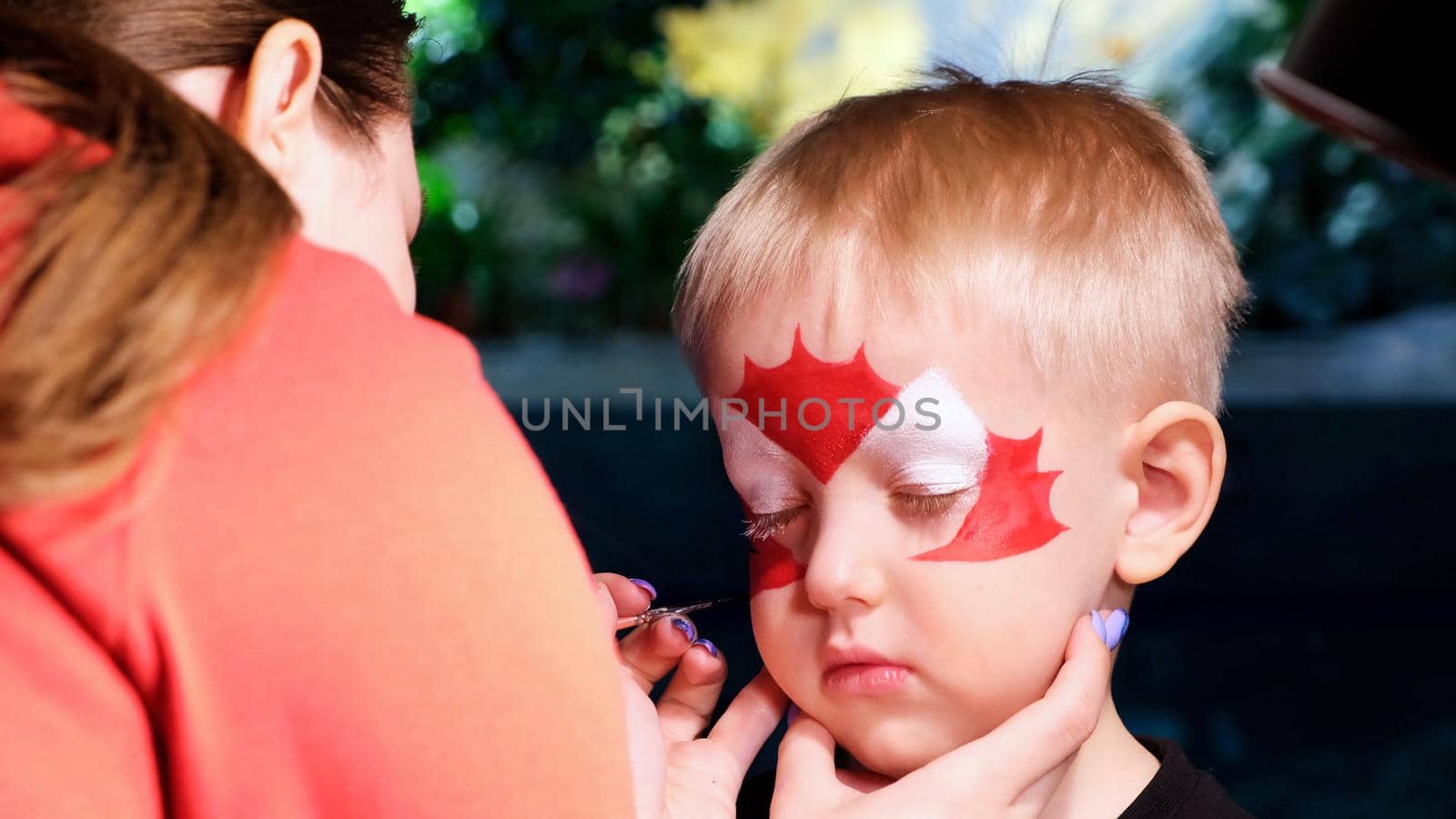 A little boy is put face painting on his face, his face is painted with paint. The concept of children's holiday, childhood, entertainment event, Halloween.
