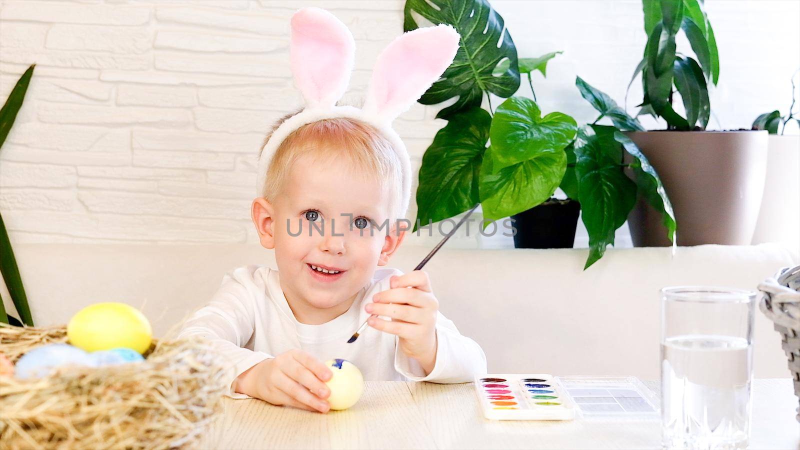 A little boy in rabbit ears enthusiastically paints Easter eggs with paint. Religious holidays concept, do it yourself, family leisure, easter egg hunt by chelmicky
