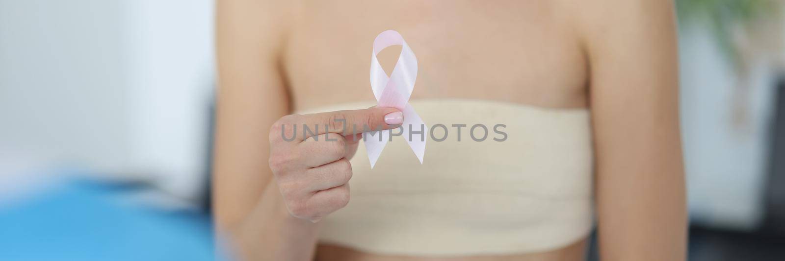 Close-up of woman hand holding symbol of breast cancer, timely diagnosis, support of oncology patients. Female health check awareness. Hospital, mammography, cancer concept. Blurred background