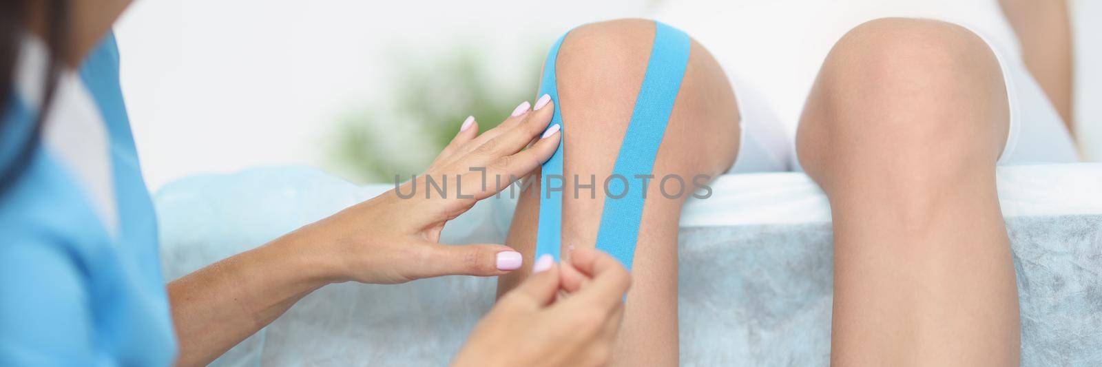 Close-up of physiotherapist applying kinesiology tape to patient knee, kinesiology taping. Post traumatic rehabilitation, sport physical therapy, medicine, healthcare concept