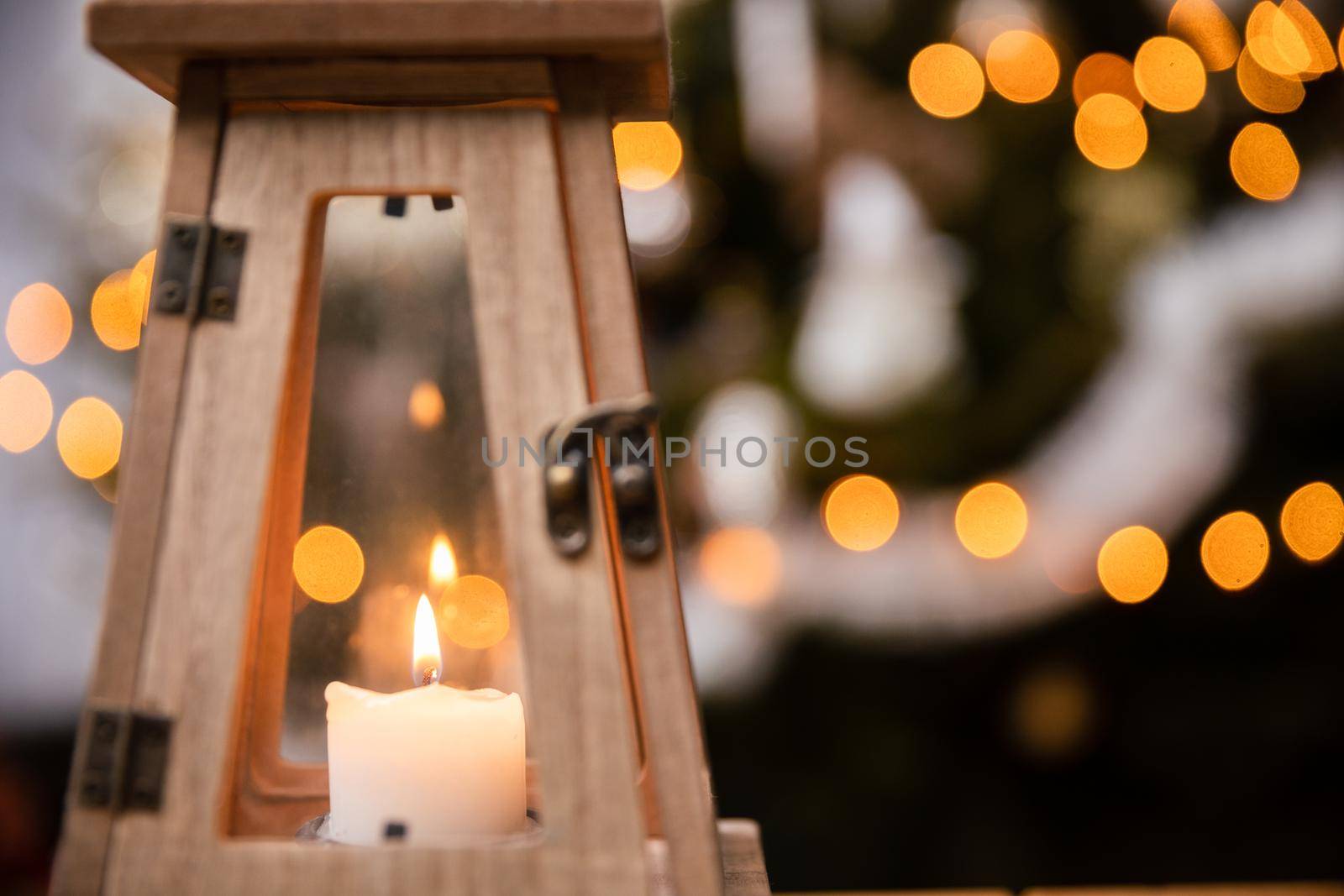 The peaceful flame of a burning candle against a background of fuzzy Christmas tree lights. Christmas atmosphere of the holidays in December.