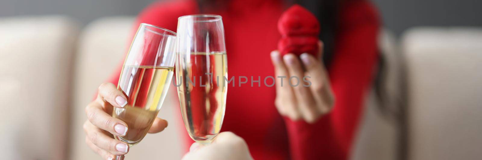 Close-up of couple on romantic dinner, man and woman raise toast with champagne flutes, man proposed to girl, red box with ring. Love, dinner, relationship, spouse, date concept. Blurred background