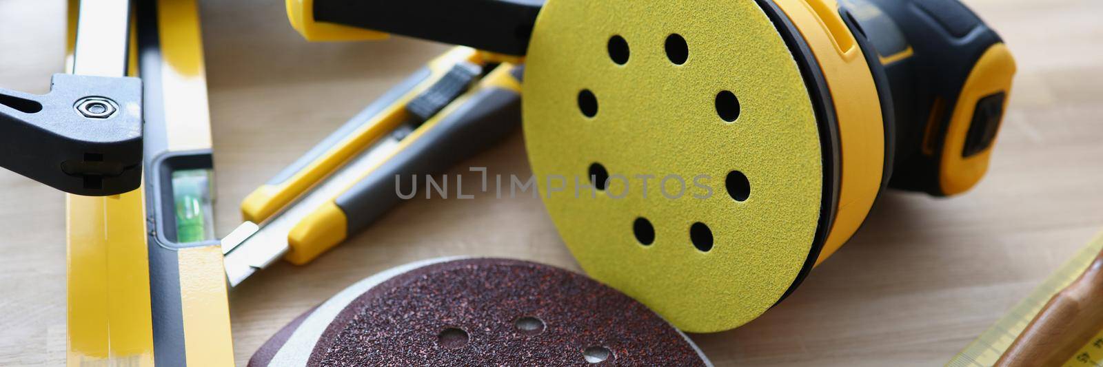 Close-up of workers instruments for repairing, equipment for work. Sanding machine, level, ruler, box cutter on wooden surface. Construction, builder, renovation, carpenter concept