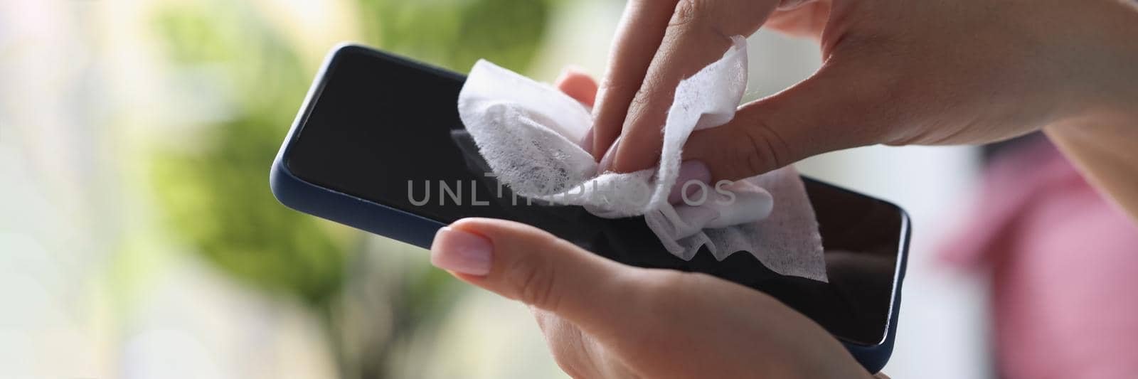Close-up of cleaning mobile phone screen with wet wipe, antibacterial and disinfecting wipe. Protective glass on smartphone screen. Technology, cleaning, prevent virus concept. Blurred background