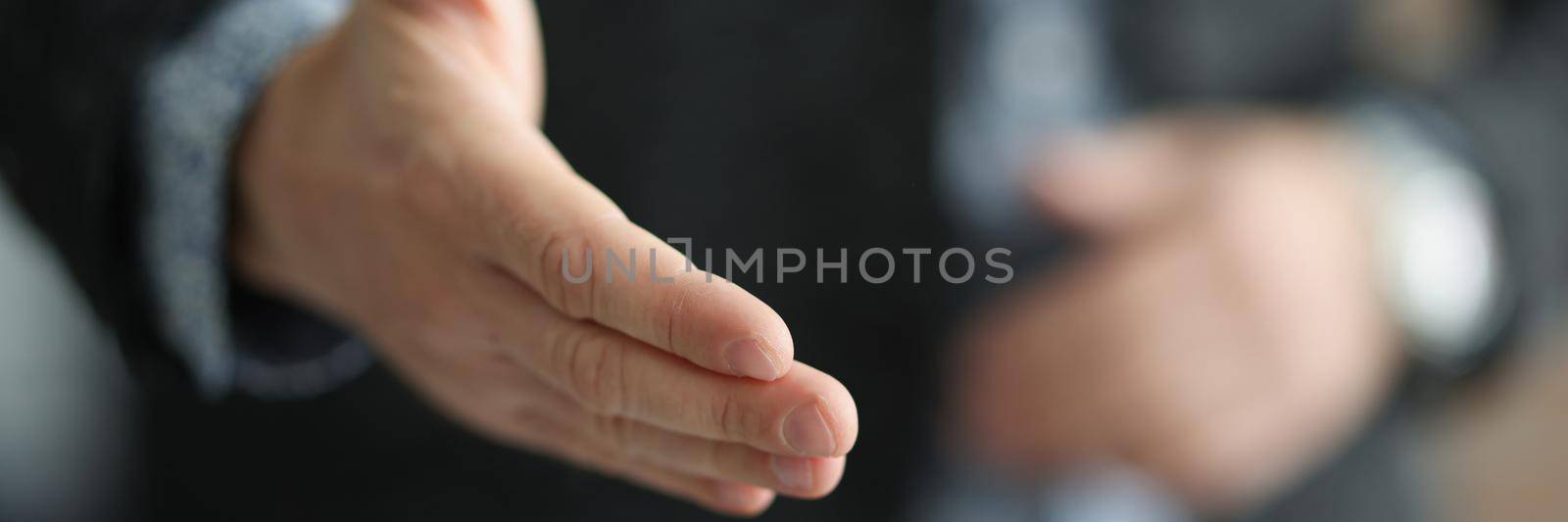 Close-up of man extending hand for handshake, greeting, offering cooperation, welcoming at job interview. Gesture of confirm agreement, successful negotiation concept. Blurred background