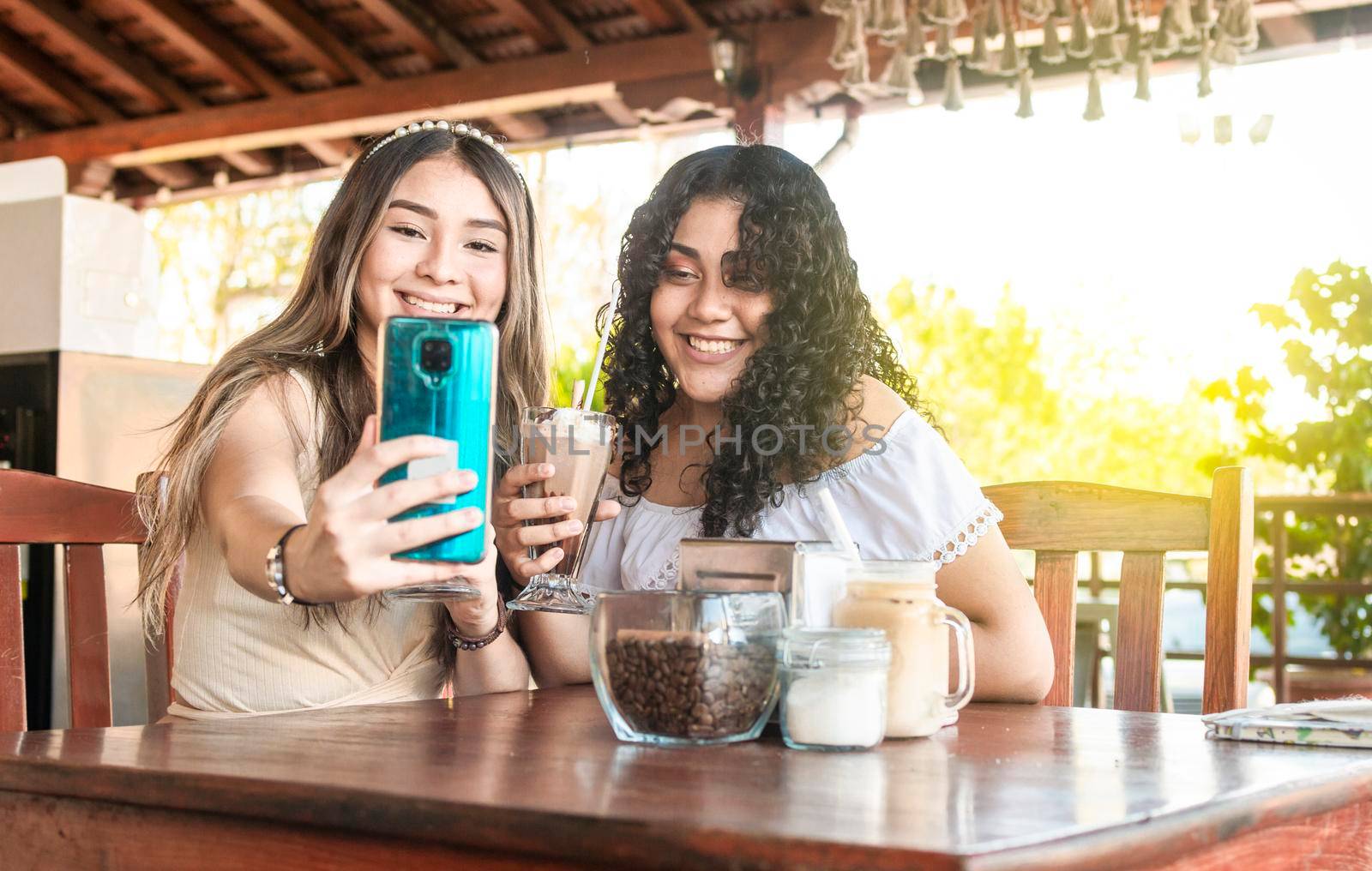 Two girls taking a selfie and drinking coffee, two girls friends in a coffee shop taking a selfie by isaiphoto