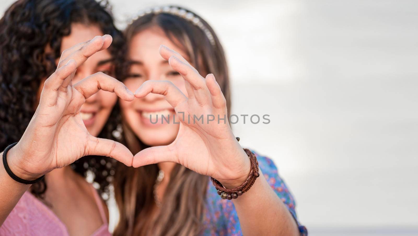 Close up of two girls making a heart shape, two friends together forming a heart, love hands sign by isaiphoto
