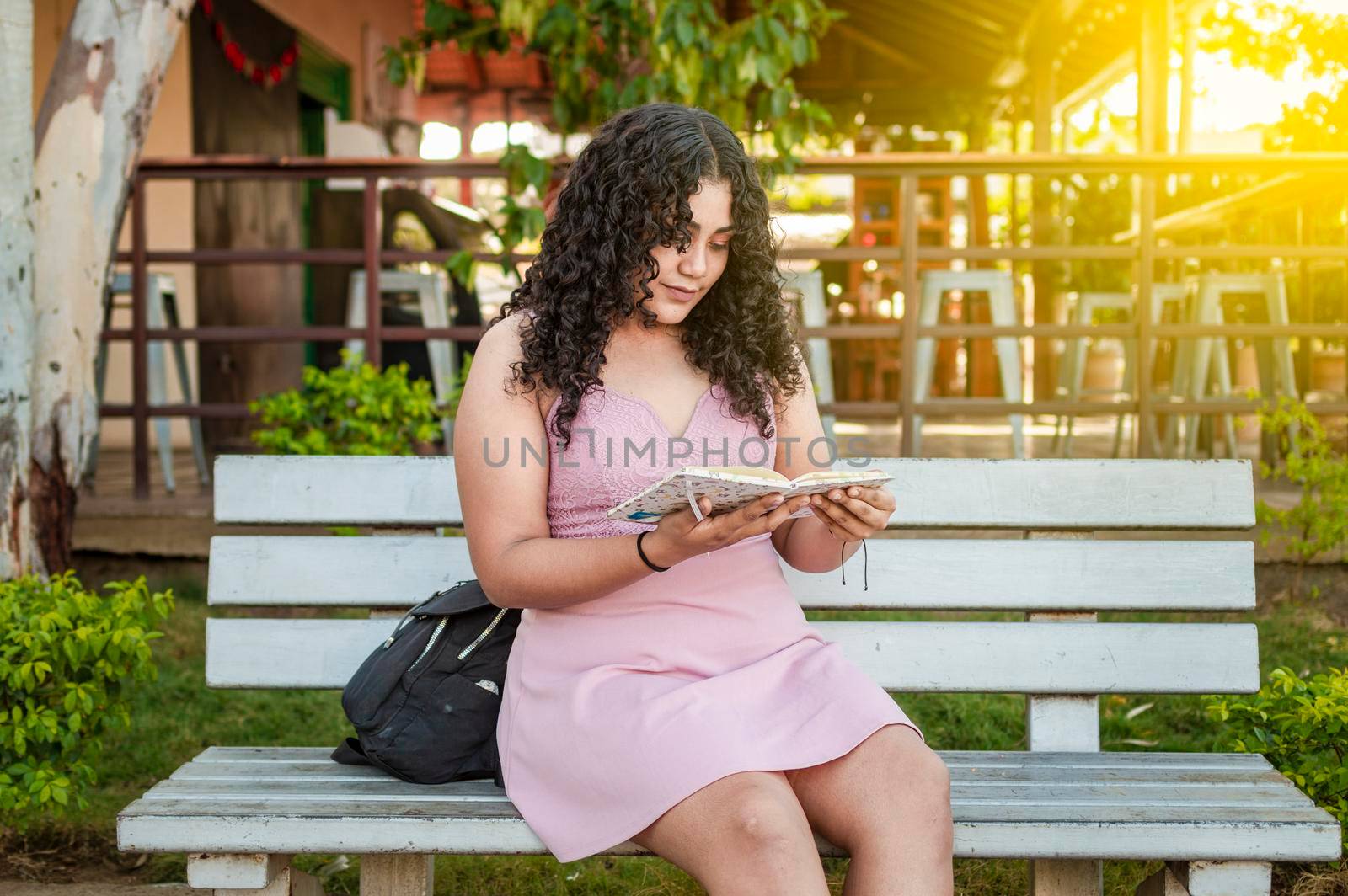 A cute girl sitting on a bench reading a book, pretty young latin girl reading a book on a bench by isaiphoto