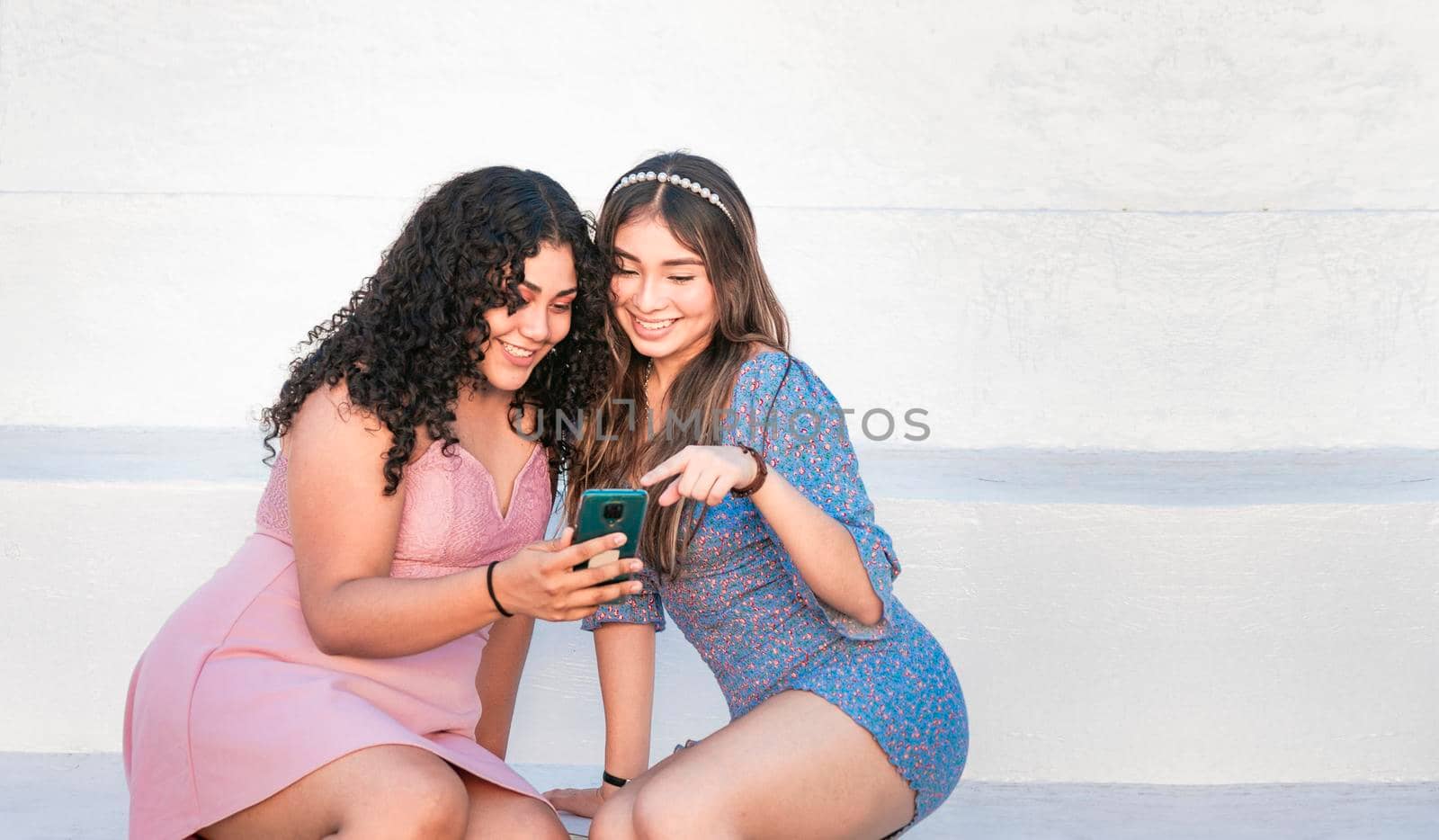 Two girls pointing at her cell phone, Girl showing her smartphone to her friend, girl checking her cell phone with her friend by isaiphoto