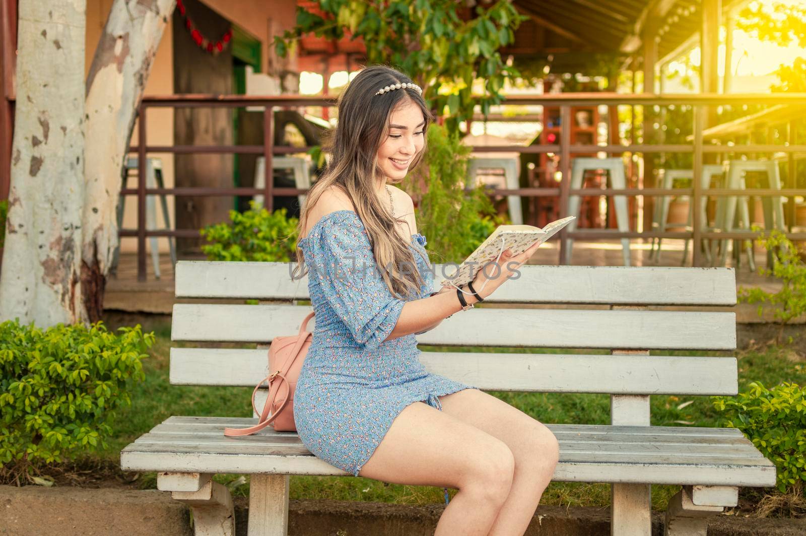 A cute girl sitting on a bench reading a book, pretty young latin girl reading a book on a bench by isaiphoto