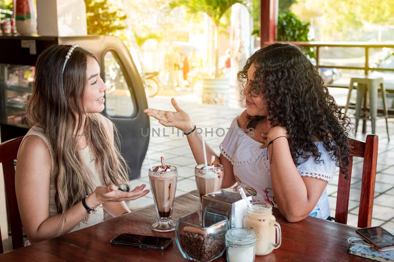 Two cute girls having a conversation in a coffee shop, two female friends discussing ideas in a coffee shop. by isaiphoto