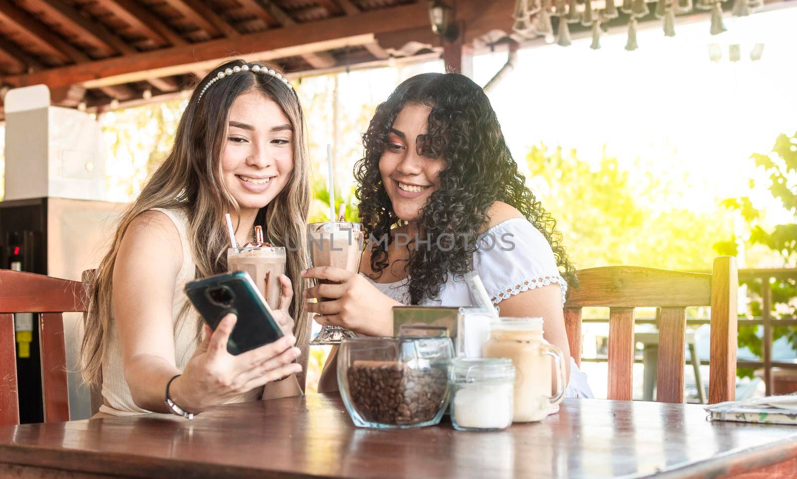 Two girls taking a selfie and drinking coffee, two girls friends with the cell phone in a coffee shop
