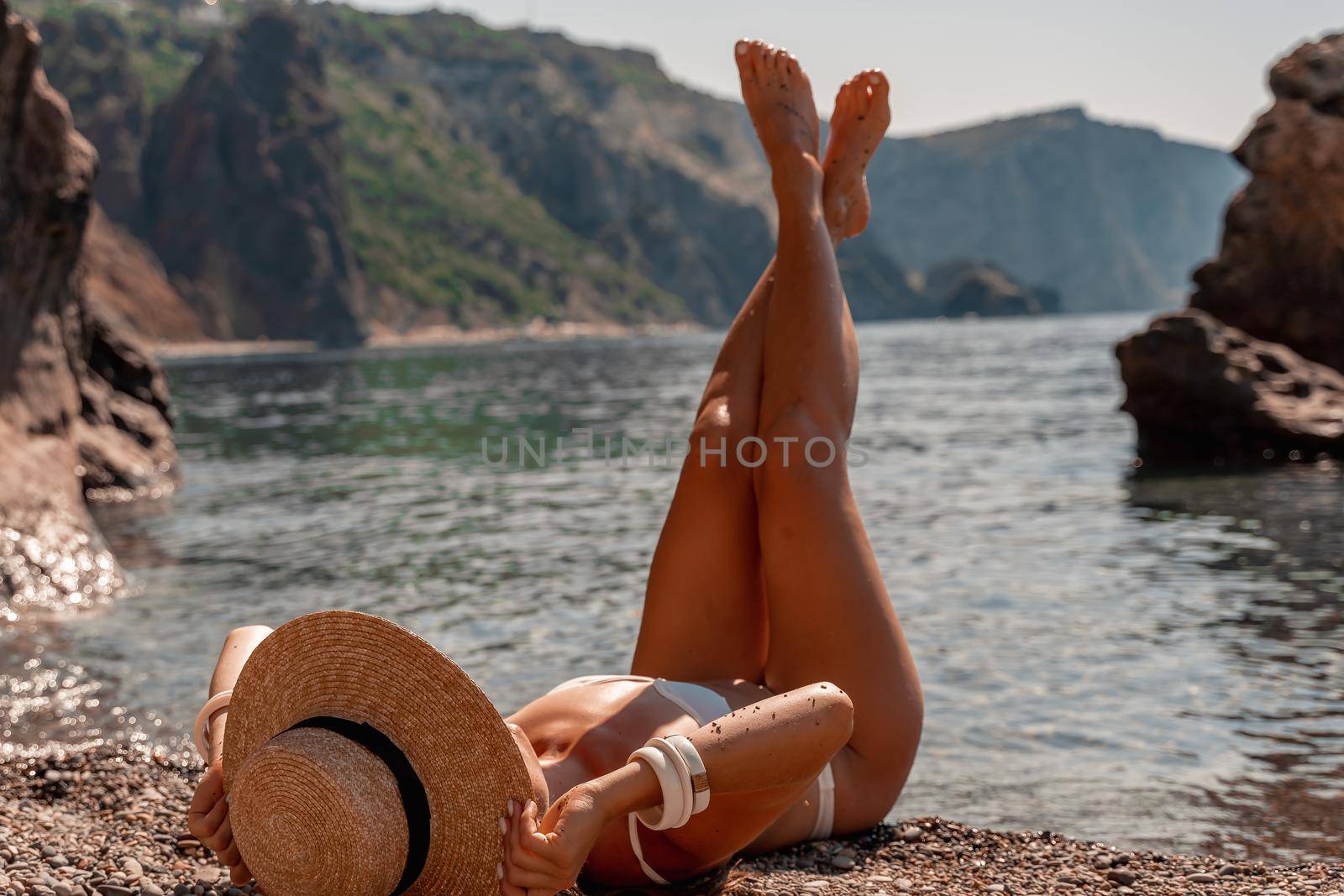 A beautiful middle-aged woman lies on the beach with her feet to the sky, covering her body with a wide-brimmed straw hat. She is sunbathing on the ocean. Vacation, travel, vacation concept. by Matiunina