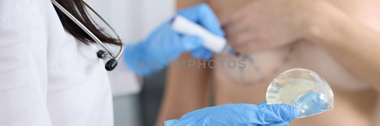 Plastic surgeon holding silicone breast implant and applying preoperative markings to patient chest closeup by kuprevich