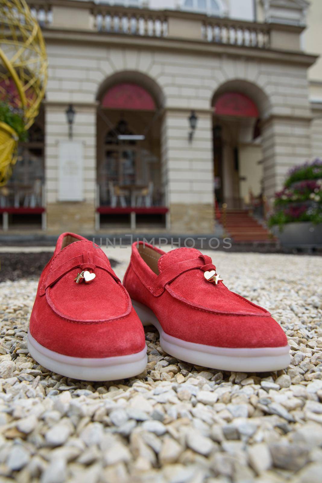 Woman's red stylish suede loafer shoes on the stone background. Pair of trendy female loafers shoes, outdoors. buildings on a background